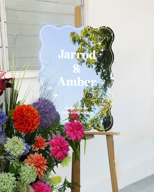 Colorful flowers on a stand with a decorative mirror and 'Jarrod & Amber' text.